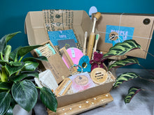 Load image into Gallery viewer, An open recyclable cardboard gift box containing various eco-friendly spa and beauty items, such as a bamboo toothbrush, wooden comb, and other personal care products, with a 'Purple Turtle' brand tag visible.